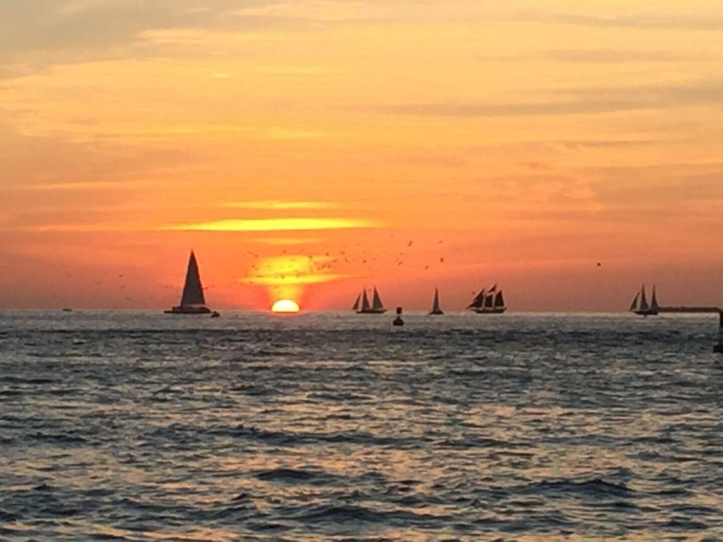 A sunset with boats in the ocean and a sail boat.