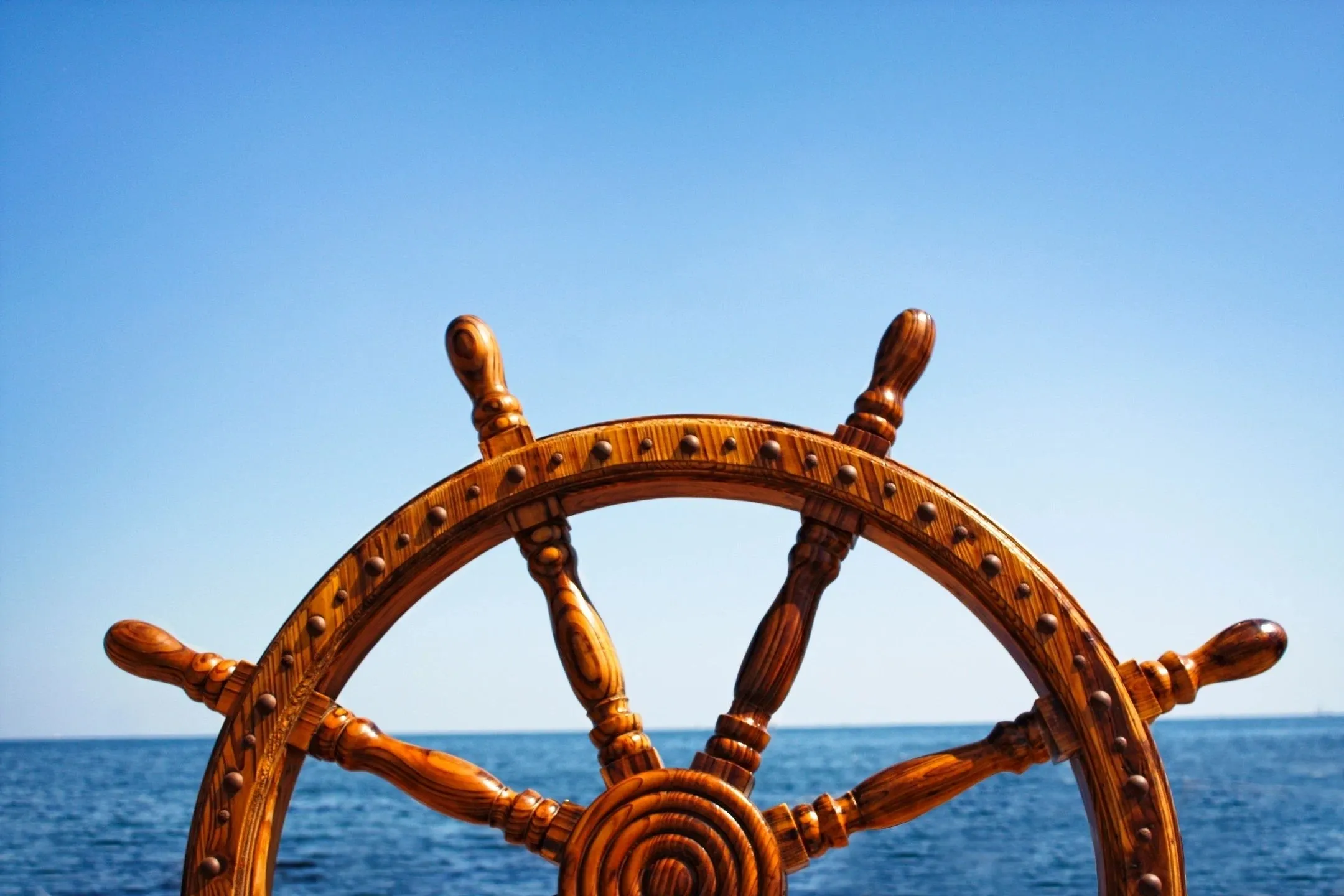 A wooden steering wheel on the ocean with blue sky in background.