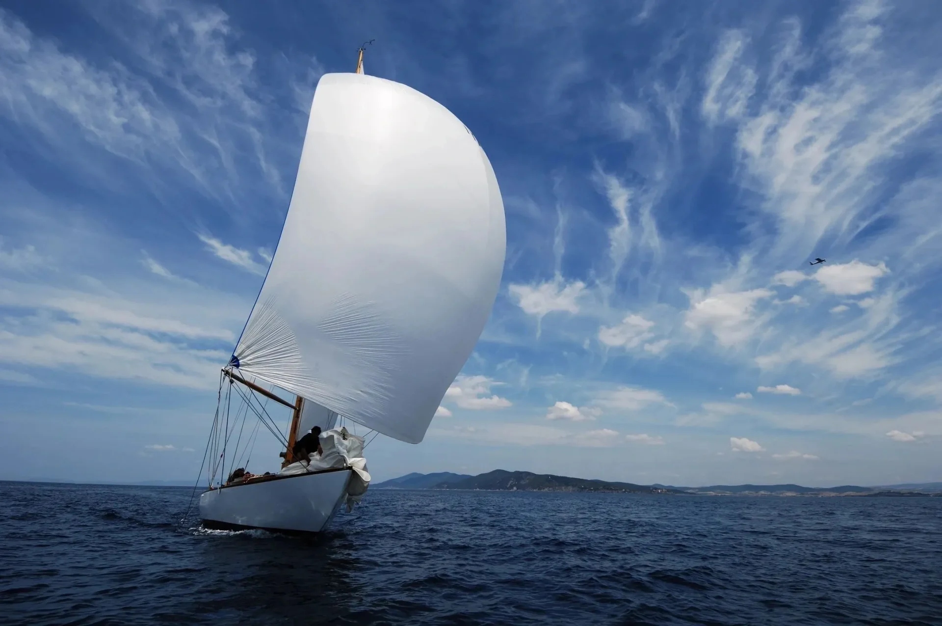 A sail boat sailing on the ocean under a cloudy blue sky.